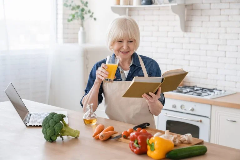 Older woman drinking orange juice and reading a book.